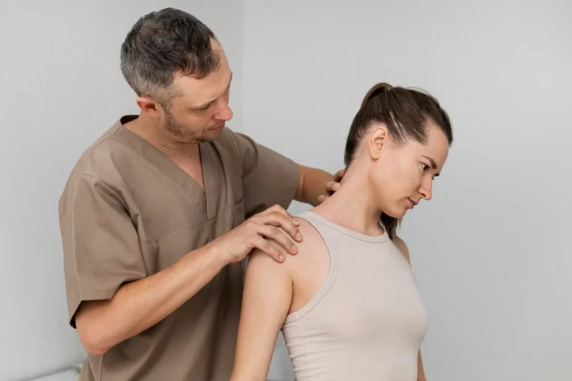Fisioterapeuta realizando una evaluación de la postura de una mujer, enfocándose en la zona del cuello y los hombros, en un consultorio de salud.