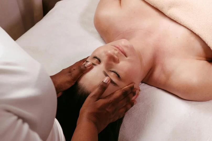 Mujer recibiendo un masaje facial relajante en un spa, mientras una terapeuta aplica técnicas de masaje en su rostro.
