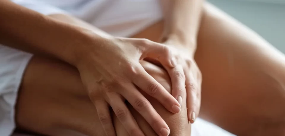 Persona tocándose la rodilla, mostrando signos de dolor o incomodidad, en un ambiente interior iluminado.