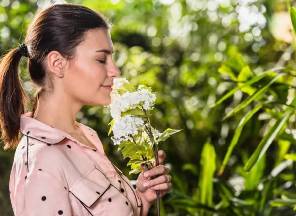 2148068647 Mujer oliendo una flor blanca en un entorno natural, rodeada de vegetación. La imagen transmite tranquilidad y conexión con la naturaleza.
